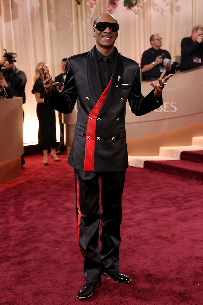 Man in black suit with red accents posing on the red carpet showcasing a bold red carpet fashion look at the 2026 Golden Globes.
