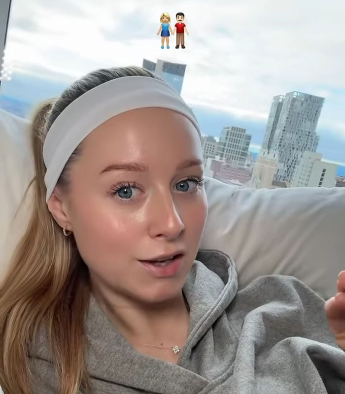 Young woman indoors with headband sharing story about having seven parents, cityscape visible through window behind her