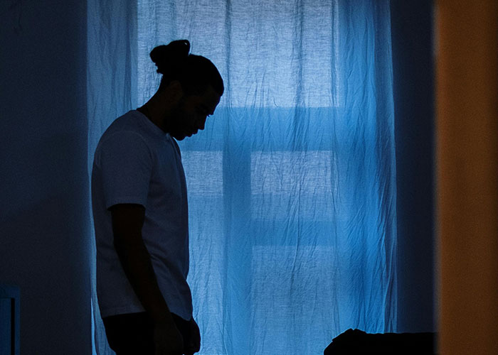 Silhouetted man standing alone in a dimly lit room, reflecting on life after discovering he is not the biological parent.