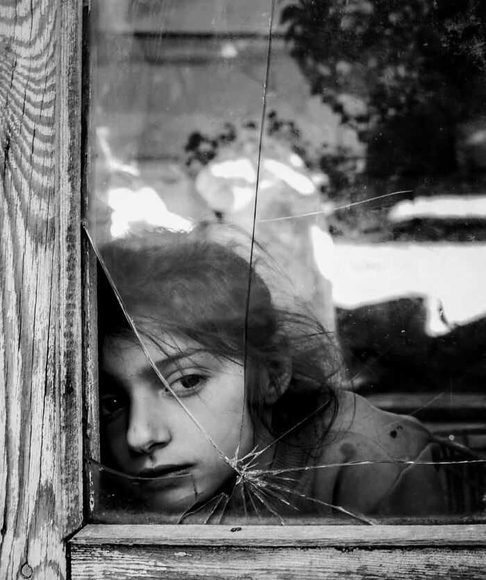 Young woman looking through a c*****d window in a black and white street photo capturing unexpected and beautiful moments.