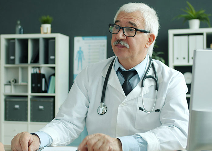 Senior male doctor wearing glasses and a stethoscope, sitting in an office discussing worst things medical professionals said