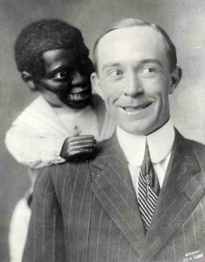 Vintage black and white photo of a man in a suit with a creepy doll on his shoulder, capturing odd and creepy vibes.