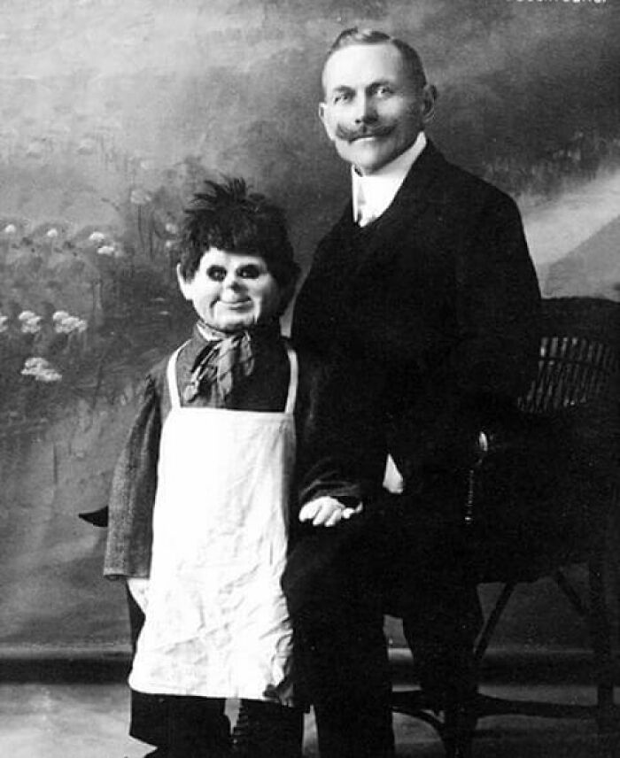 Vintage black and white photo of a man posing with an odd and creepy ventriloquist dummy in an old studio.