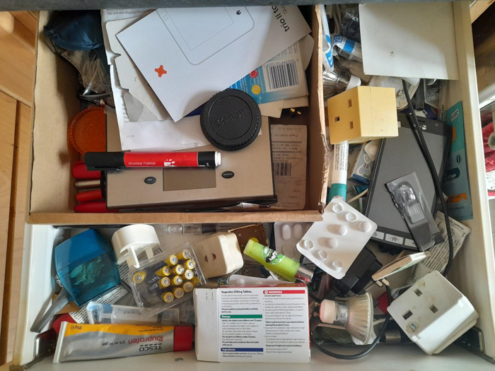 Cluttered drawer with random items including medication, batteries, chargers, and small gadgets representing disorganized New Year’s resolutions ideas.