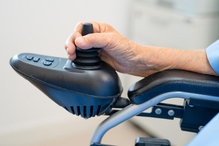 Close-up of a hand controlling a wheelchair joystick, highlighting unusual public behavior with zero shame.