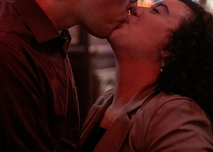 Couple sharing a close kiss in a dimly lit setting, capturing a moment of intimate revenge acts and secrecy.