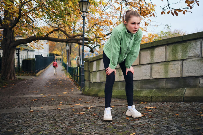 Young woman in a green jacket catching her breath after exercise on a leafy autumn path showing moment that hits harder than expected
