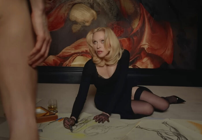 Madonna in a raunchy Dolce & Gabbana ad sketching a male model with a c****h shot, surrounded by younger men.