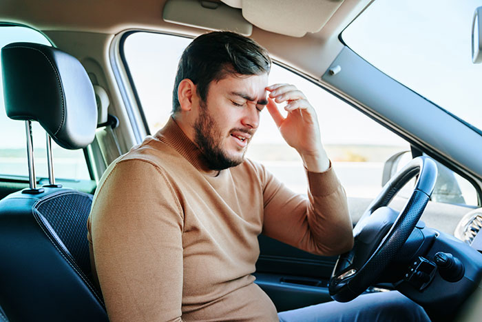 Man sitting in the driver&rsquo;s seat of a car, holding his head in frustration after an anxiety meltdown risk situation.