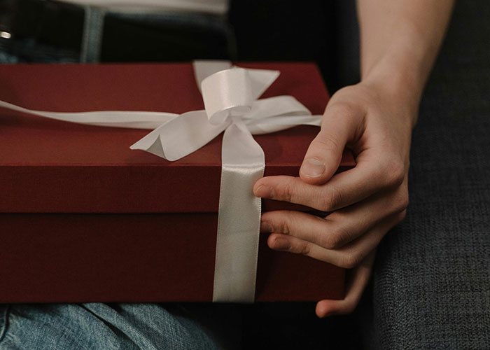 Close-up of a woman holding a red gift box tied with a white ribbon, reflecting on ungrateful feelings and abhorrent gifts.