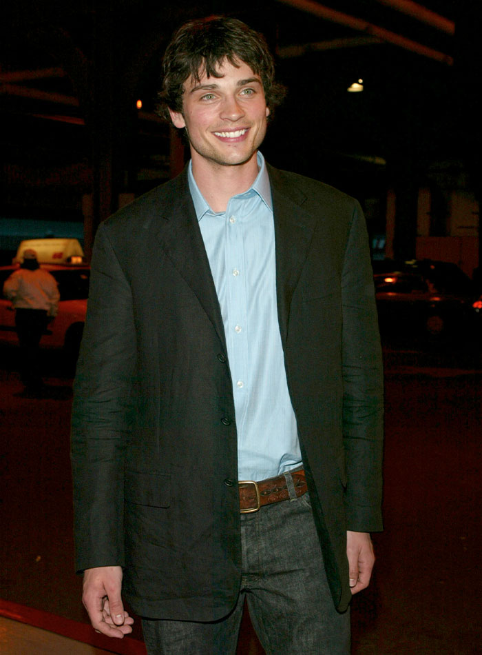 Young 2000s teen heartthrob smiling, wearing black blazer and blue shirt at an evening event outdoors.