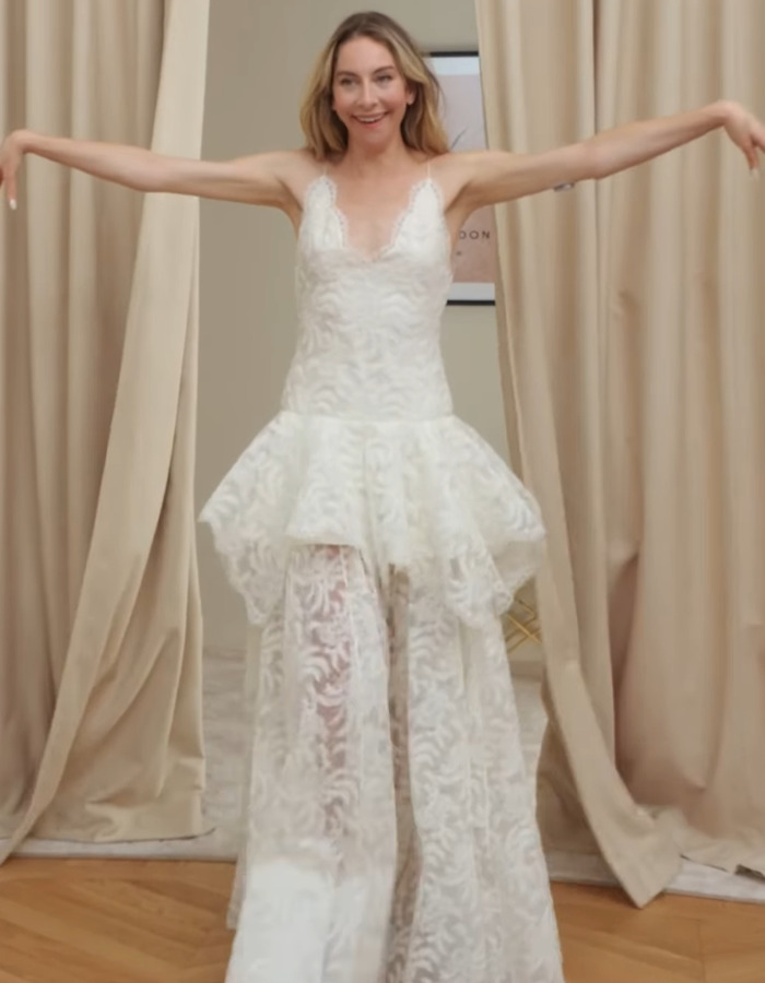 Woman in a white lace dress with sheer pants, posing with arms outstretched, wedding look scrutinized by fans.