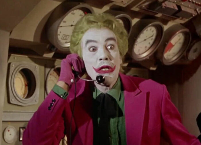 Actor in joker makeup and colorful costume on movie set speaking on a headset, representing diva stars and movie set workers.