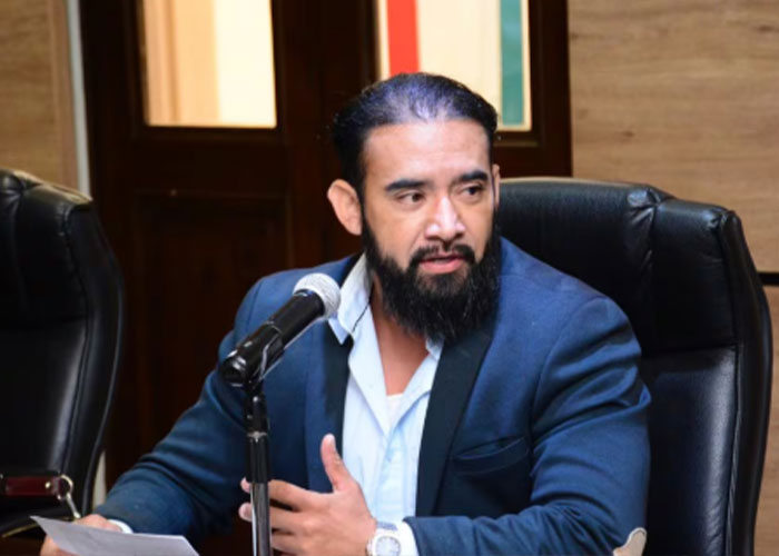 Man with beard in a blue suit speaking into a microphone during a formal discussion on gender identity and child support issues.