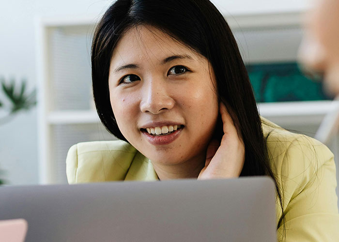 Young woman with long dark hair sitting behind a laptop, engaging in a conversation about neurodivergent habits.