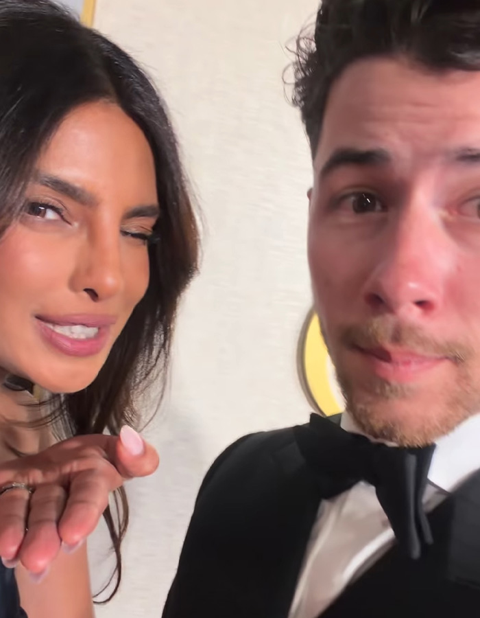 Nick Jonas at Golden Globes 2026 event, dressed in a tuxedo, with a woman winking and blowing a kiss.