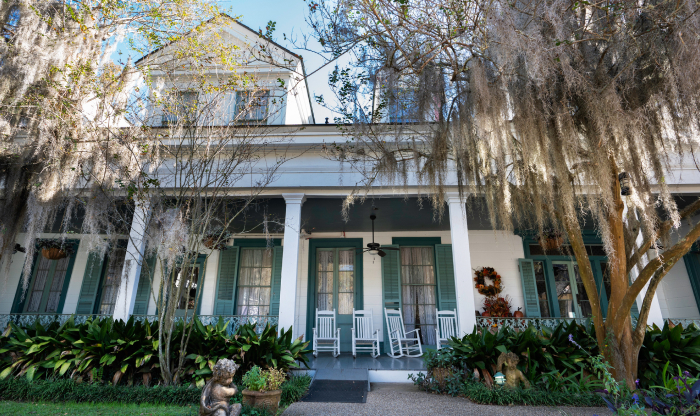 Historic southern plantation house with rocking chairs surrounded by moss-draped trees in a haunted place setting.