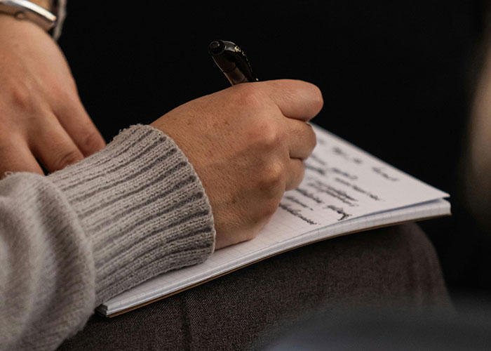Person wearing a gray sweater writing notes in a notebook, illustrating neurodivergent experiences and personal reflections.
