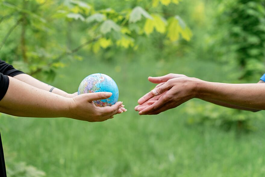 Person passing a small globe to another person, illustrating the concept of Earth cost and value.