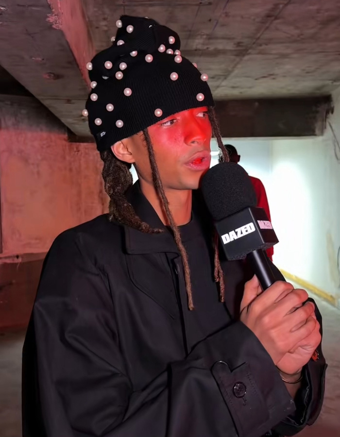 Jaden Smith in a black pearl-studded hat and coat speaking into a DAZED microphone during an interview. Jaden Smith in a black pearl-studded hat and coat speaking into a DAZED microphone during an interview.
