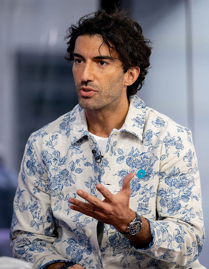 Justin Baldoni speaking during an interview, wearing a floral jacket and gesturing with his hand.