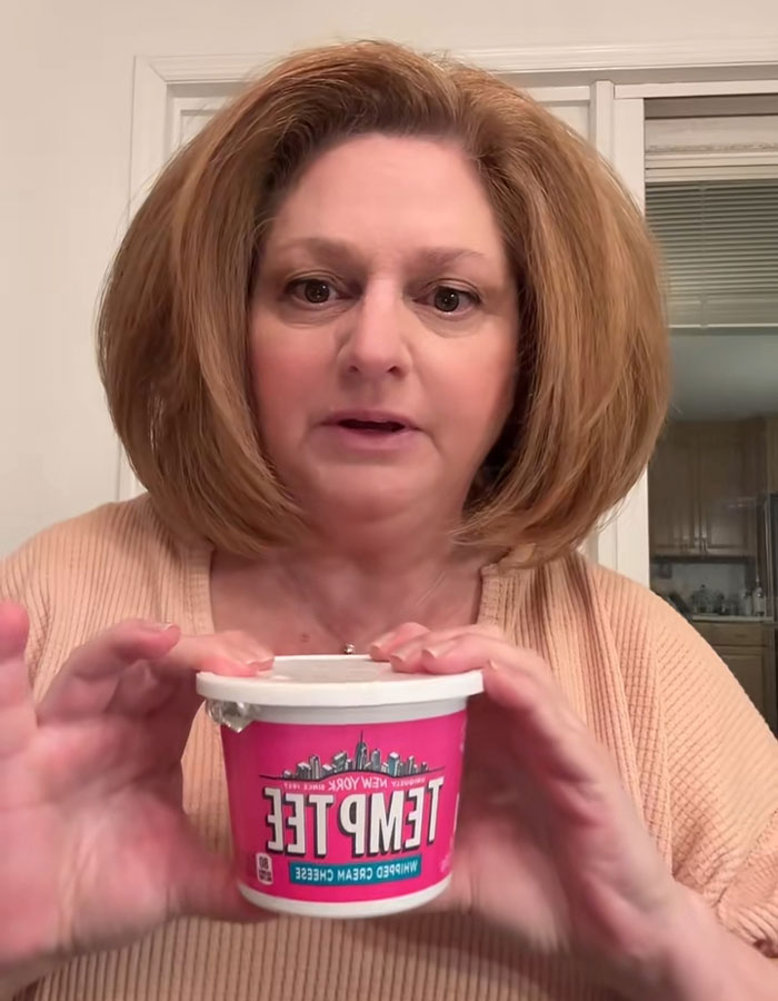 Woman holding a container of cream cheese, sharing her review that sparked internet buzz for all the wrong reasons. Woman holding a container of cream cheese, sharing her review that sparked internet buzz for all the wrong reasons.