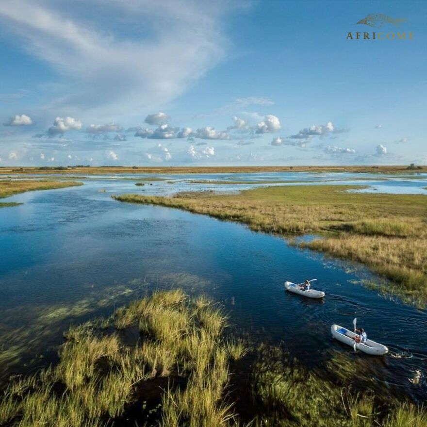 Two people kayaking on a river surrounded by grasslands under a partly cloudy sky, ideal places to visit at least once.