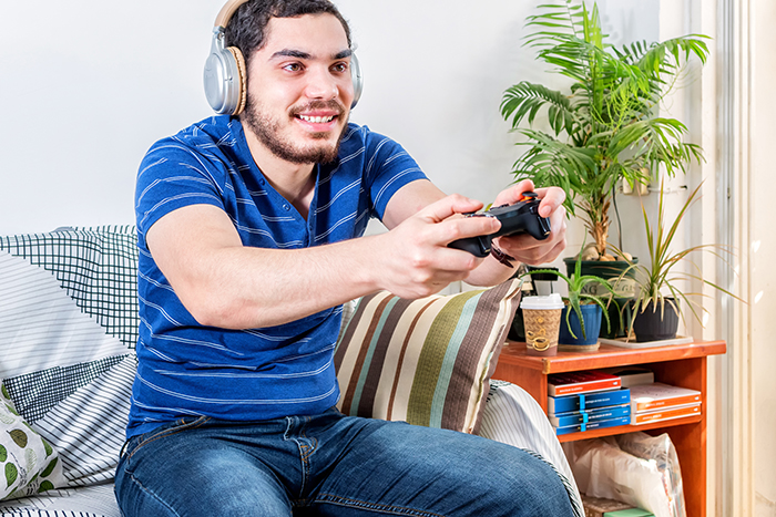 Young man playing video games at home, avoiding chores while planning to move from mom&rsquo;s house to girlfriend&rsquo;s place.