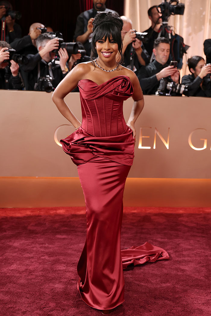 Woman in a red satin gown posing on the red carpet among photographers showcasing jaw-dropping outfits Golden Globes 2026.
