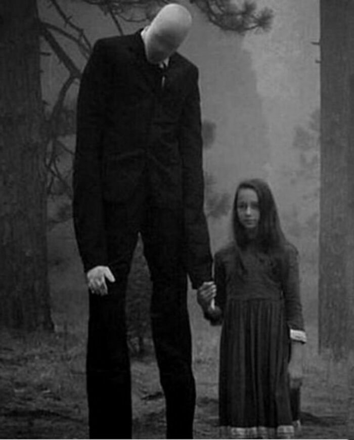 Tall faceless figure in a suit holding hands with a girl in a dress in an eerie black and white creepy scene.