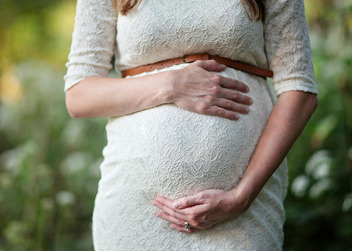 Pregnant woman in a white lace dress gently holding her belly outdoors, symbolizing parenthood and family changes.