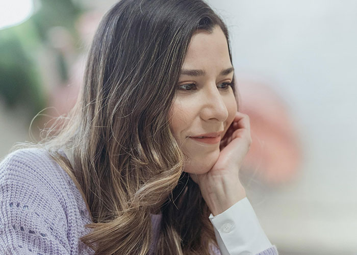 Woman with long hair wearing a purple sweater, smiling thoughtfully, representing perfect revenge acts concept.