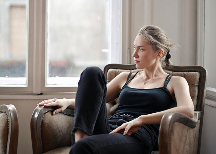 Young woman in casual clothes sitting thoughtfully on an armchair reflecting on neurodivergent experiences at home.