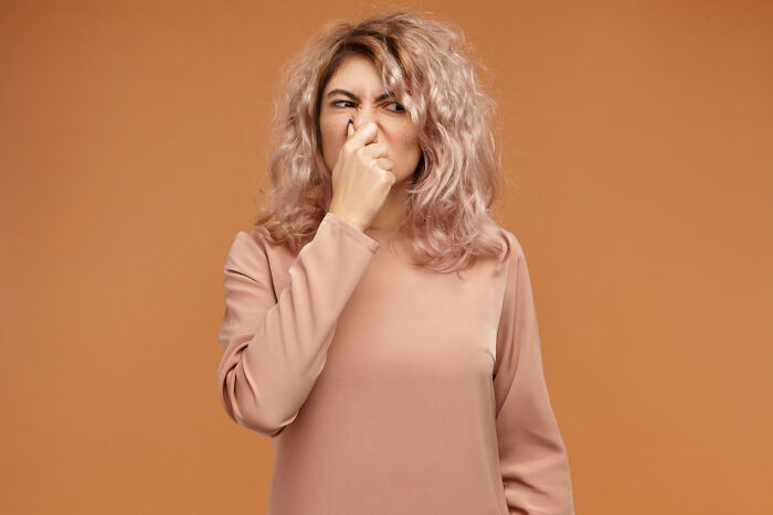 Woman with curly hair pinching nose, showing disgust, representing reaction to accidental texts causing panic moments.