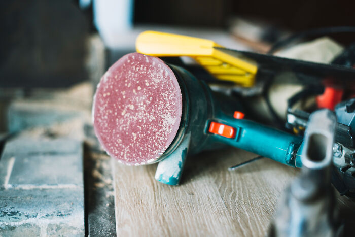 Orbital sander covered in dust on a workbench, illustrating weird and satisfying situations with a not my problem attitude.
