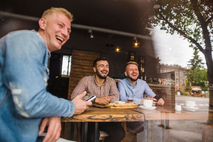 Three men laughing inside a restaurant, capturing awkward moments people in the service industry experience.