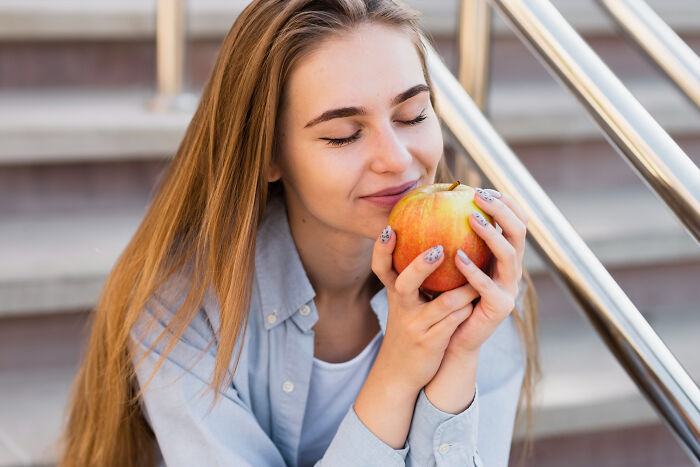 Young woman with long hair holding an apple close to her face, experiencing moments that hit people harder than expected