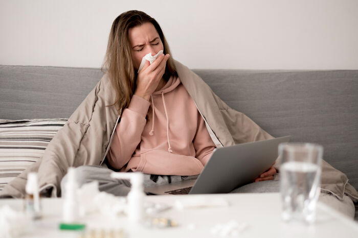 Woman sick at home wrapped in blanket using laptop, illustrating bizarre office rules causing frustration and confusion.