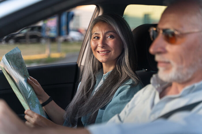 Mom looking shocked and concerned while sitting in a car with an older man, contemplating son's cheating on girlfriend situation.