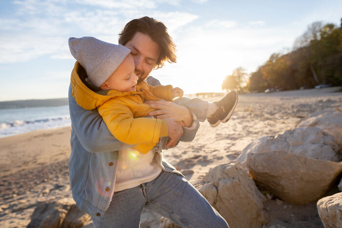 Man holding child in yellow jacket on a beach during sunset, capturing moments that hit people harder than expected