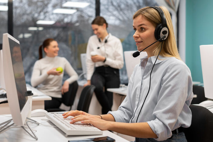 Young woman with headset working at computer in office, depicting bizarre office rules that frustrate employees.