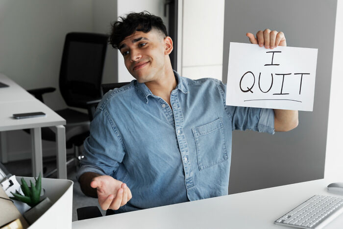 Young man in an office holding an I quit sign, illustrating satisfying situations where people say not my problem anymore.