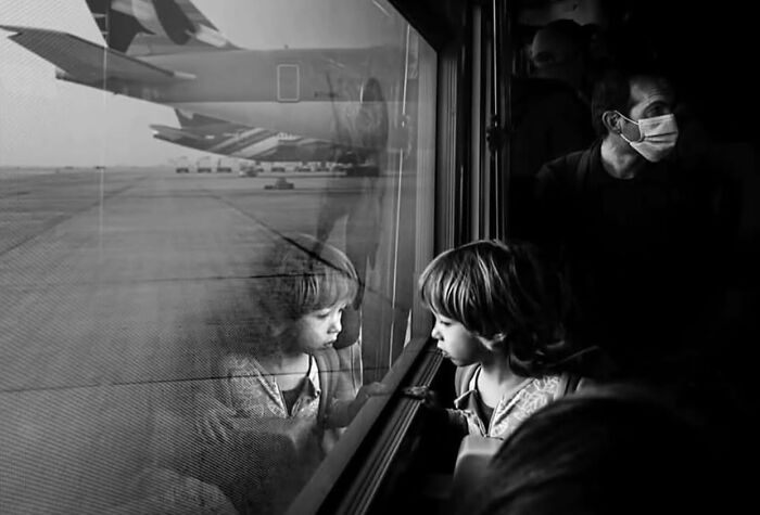 Child looking out airplane window, reflecting on life’s unexpected and beautiful moments in candid street photo.