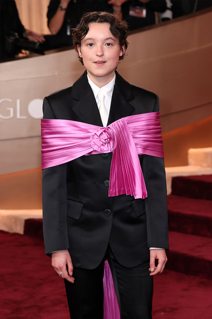 Person wearing a black suit with a large pink satin bow, showcasing a red carpet fashion disaster at the 2026 Golden Globes.