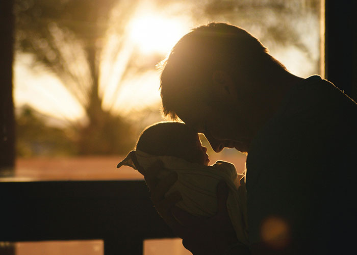 Silhouette of a man holding and looking lovingly at a baby during sunset, illustrating non-biological parenthood emotions.