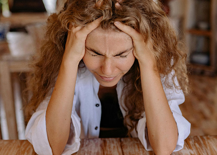 Young woman with curly hair holding her head in frustration, representing challenges of being neurodivergent.