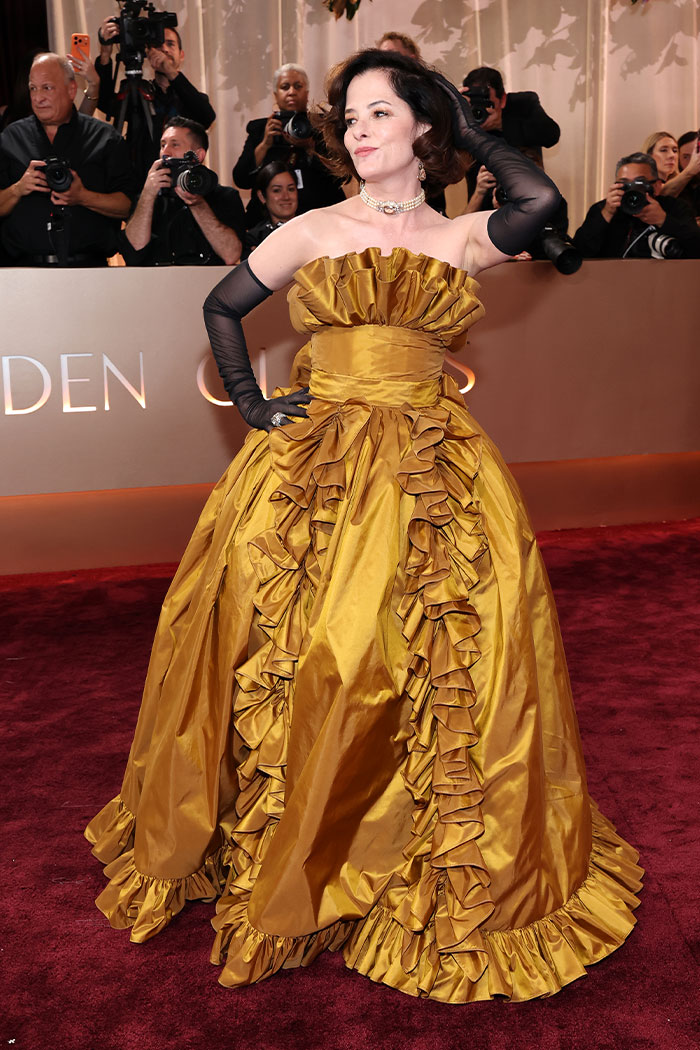 Woman posing in a ruffled gold gown with black gloves at a 2026 Golden Globes red carpet fashion disaster event.