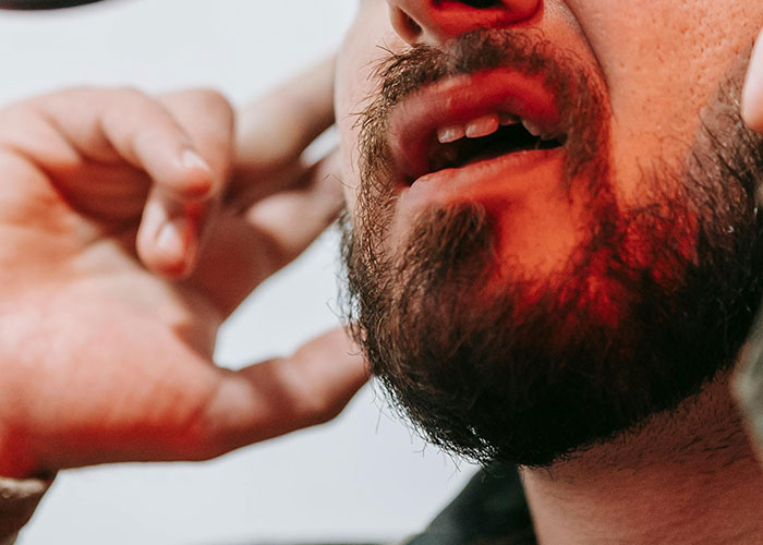 Close-up of a person with a beard touching their ear, illustrating habits neurodivergent people thought were normal.