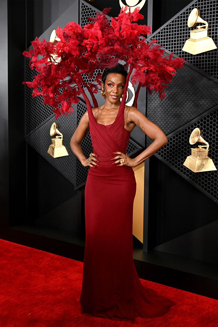 Woman in a bold red gown with extravagant floral headpiece posing on red carpet at Grammys wild fashion event.