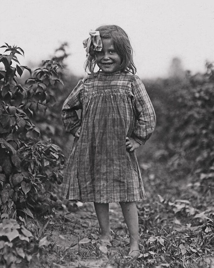 Black and white photograph of a smiling young girl in a plaid dress outdoors, showing the sad and beautiful history of humanity.